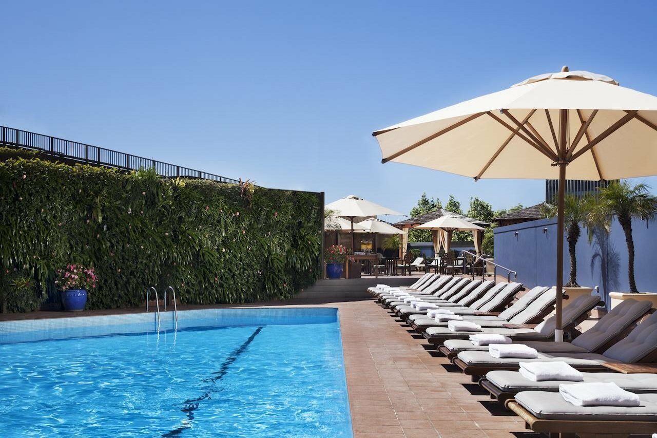 Four Seasons Hotel Sydney Létesítmények fotó The photo shows a swimming pool surrounded by lounge chairs and large umbrellas. The pool itself has clear blue water, and there is a green wall of lush vegetation nearby, providing a natural backdrop. In the background, there are additional shaded s